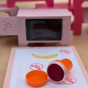 Kaufen Sie einen Bitcoin-Stempel mit orangefarbener Kappe und eine Lightning Piggy-Spardose im Hintergrund